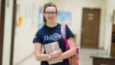 一个女学生拿着她的ipad和书包微笑着.